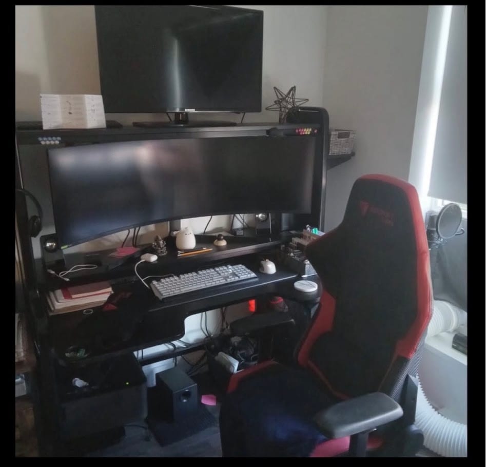 A black desk with two monitors and a red and black gaming chair.