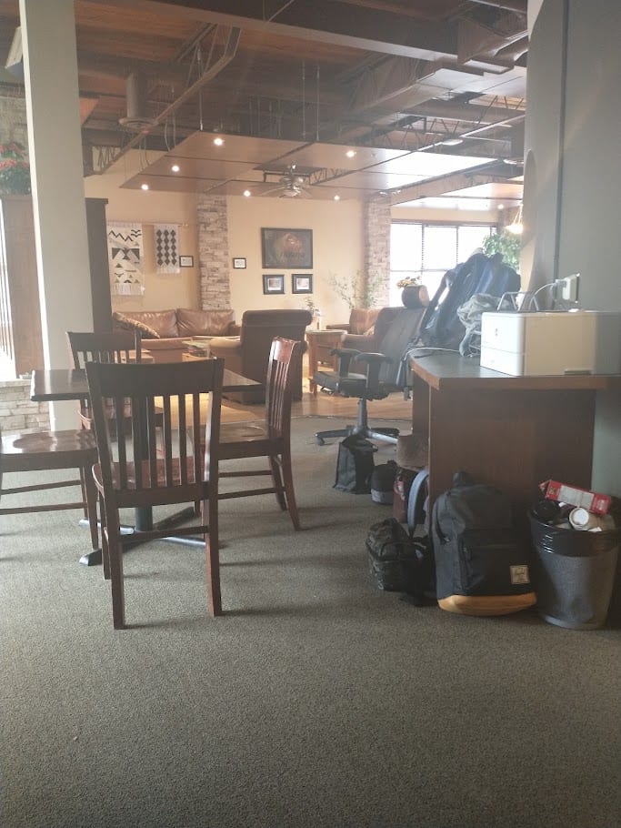 A lounge with leather sofas, wooden tables and chairs, and bags on the floor near a desk.