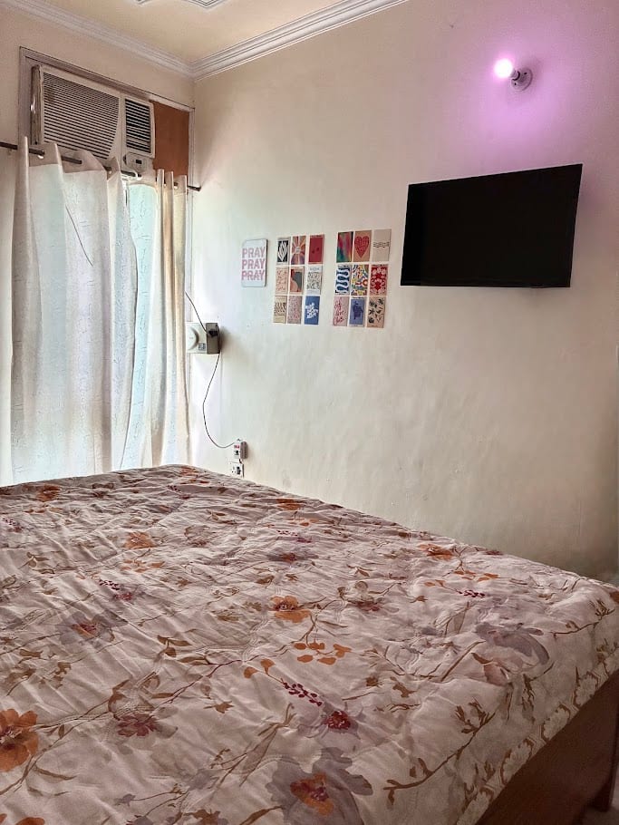A bedroom with a floral bedspread, a wall of small cards, and a television.