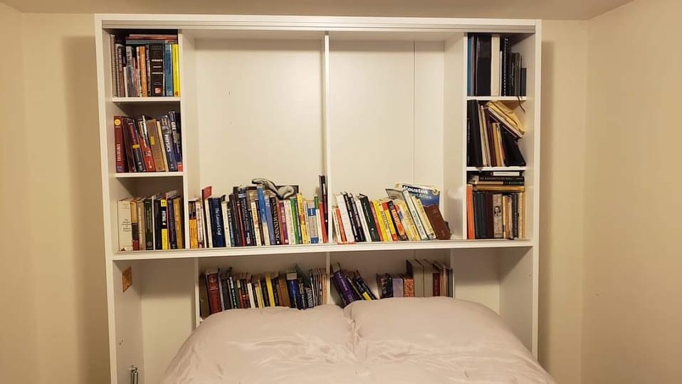 A white built-in bookshelf above a bed, with books lined along the middle shelf.