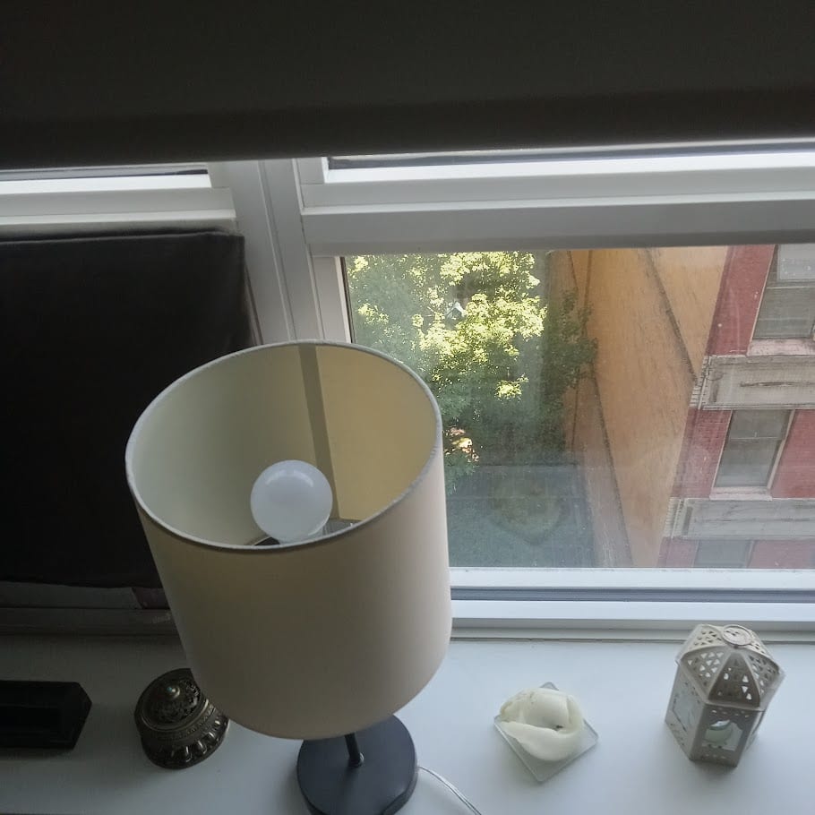 A windowsill with a lamp, a small metal jar, a white ornament and a lantern.